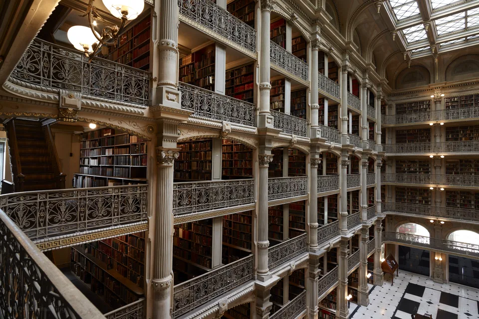 Globe lamps and ornate iron railings along a balcony of book stacks in the George Peabody Library