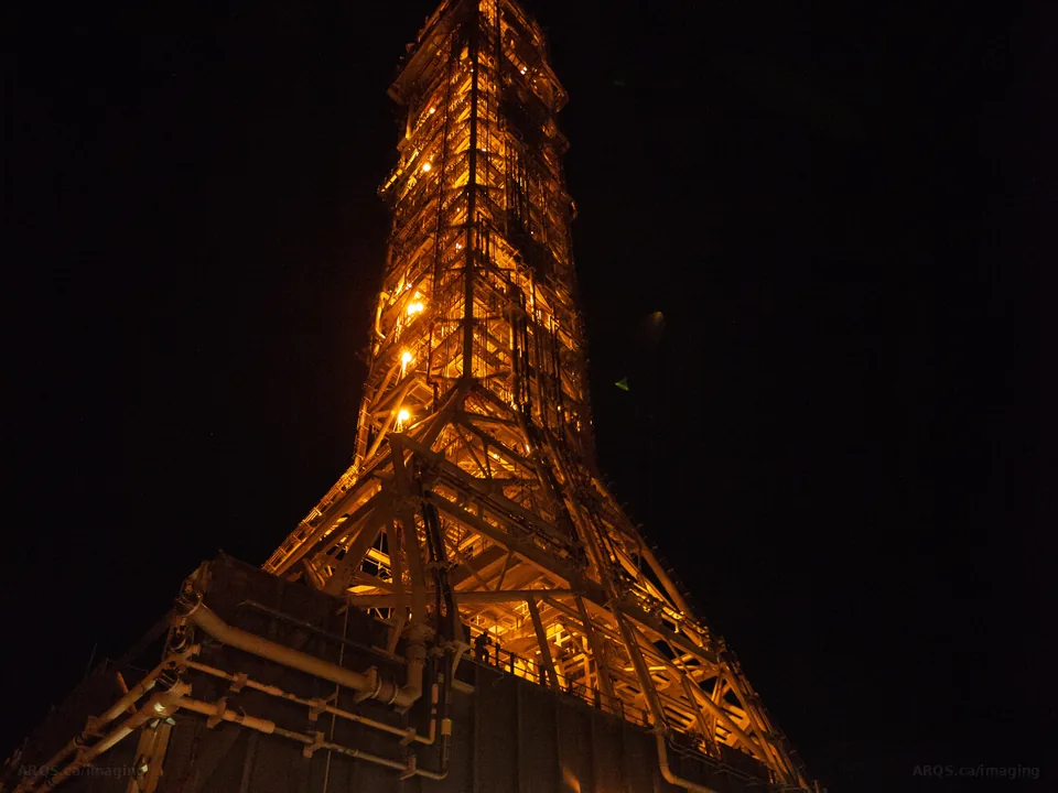 A floodlit steel launch tower glowing orange as it moves to the pad at night