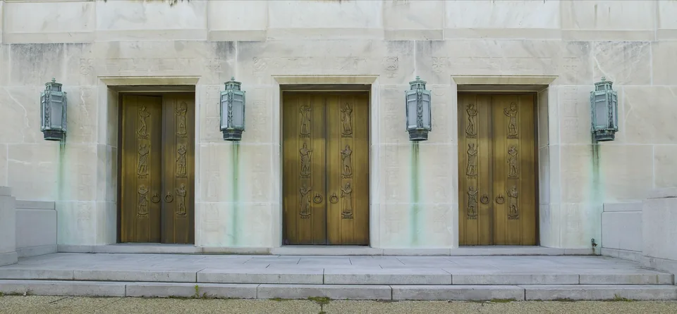 Three sculpted bronze doors by Lee Lawrie at the east entrance of the Library of Congress John Adams Building, between verdigris lanterns on a white marble wall