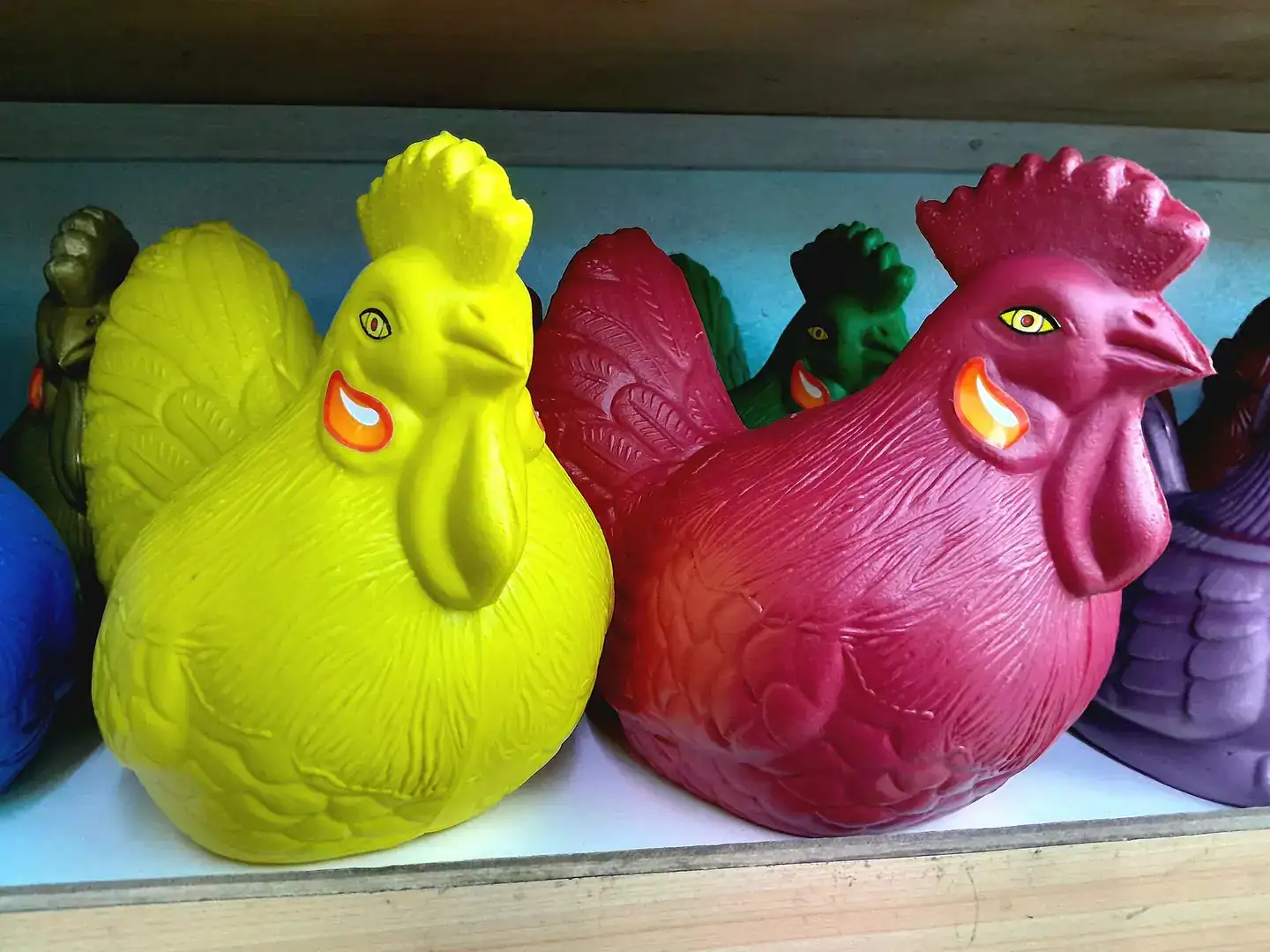 Colorful plastic chicken-shaped piggy banks displayed on a wooden shelf