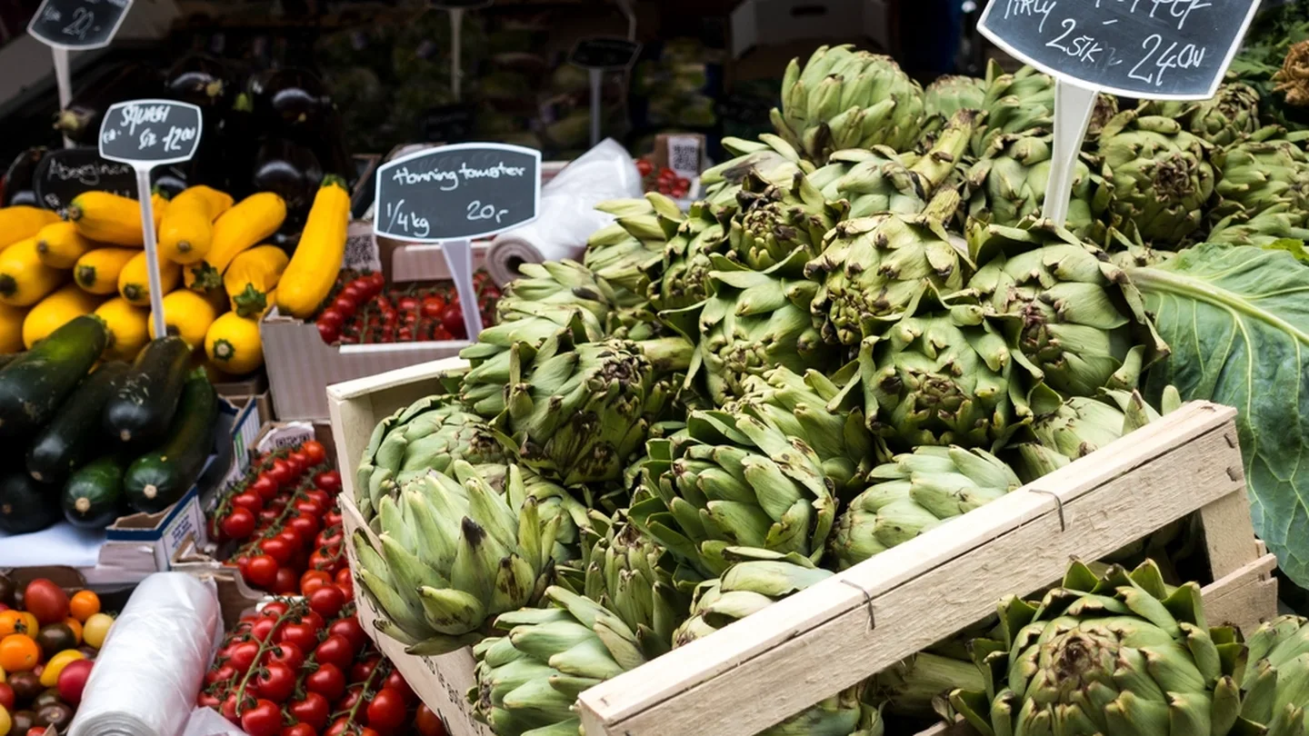 Fresh artichokes and produce stacked at a market stall