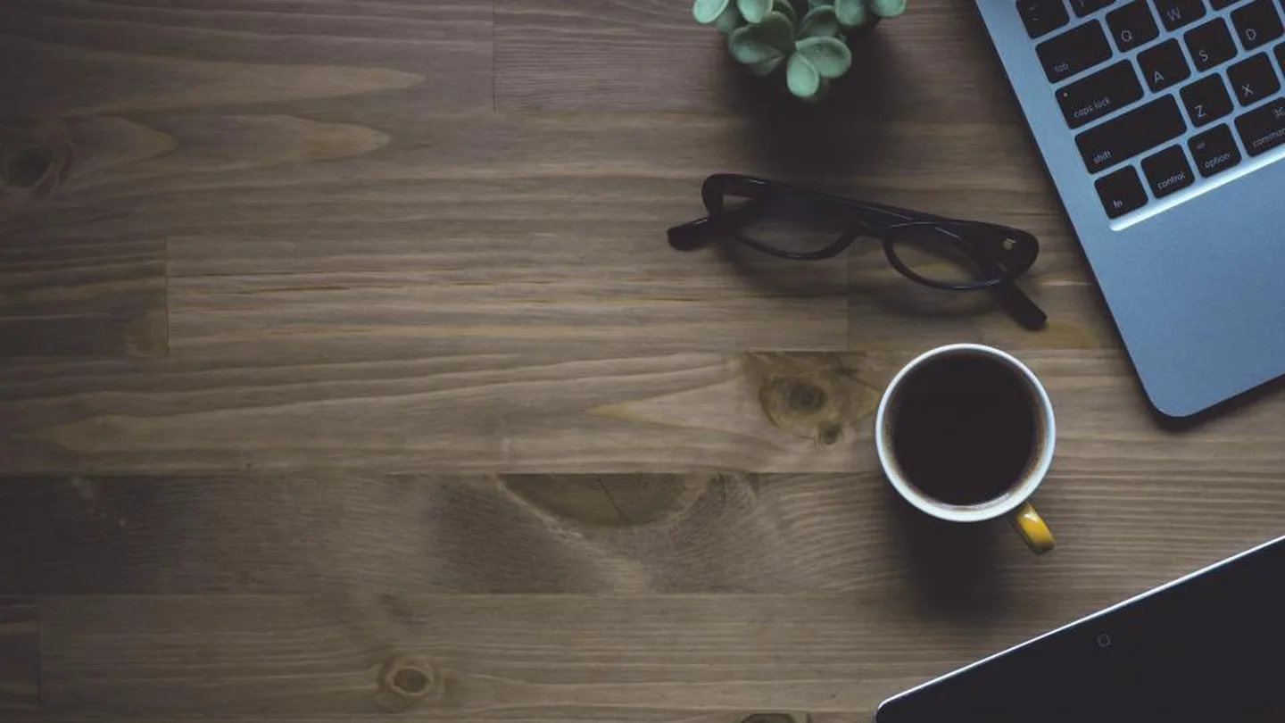 A laptop, coffee and glasses on a wooden work desk